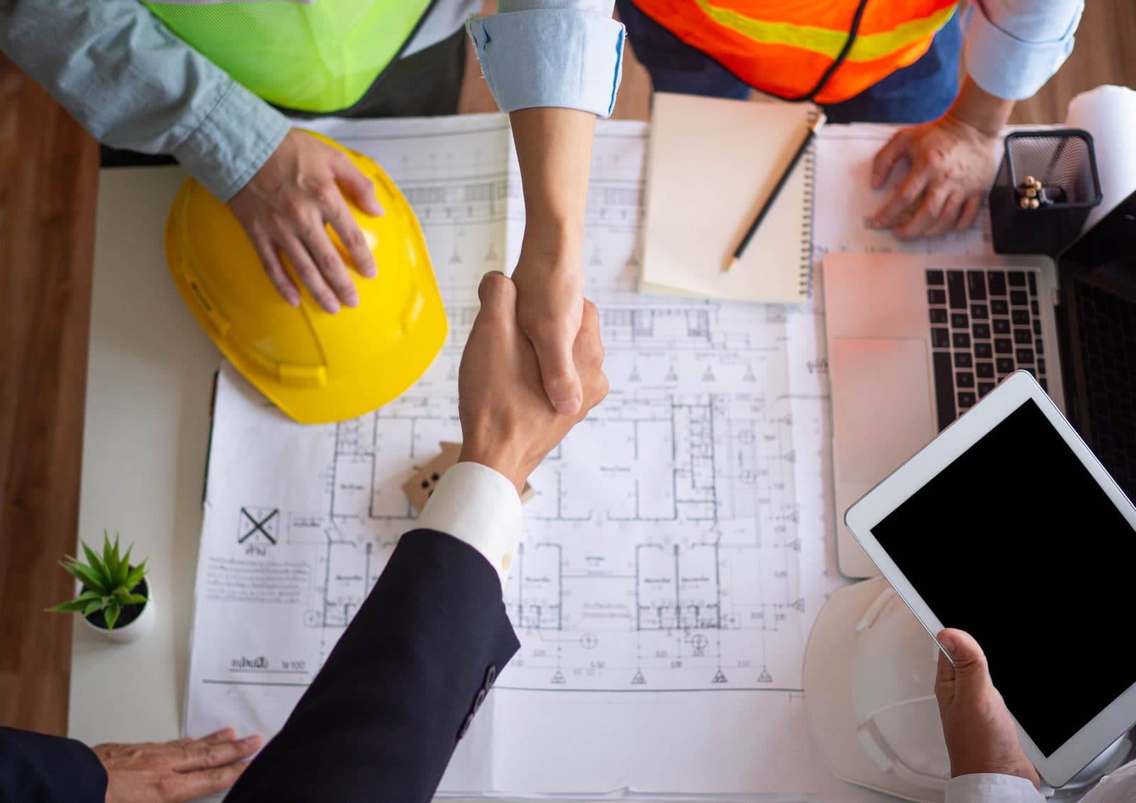 Business handshake over architectural plans and a laptop