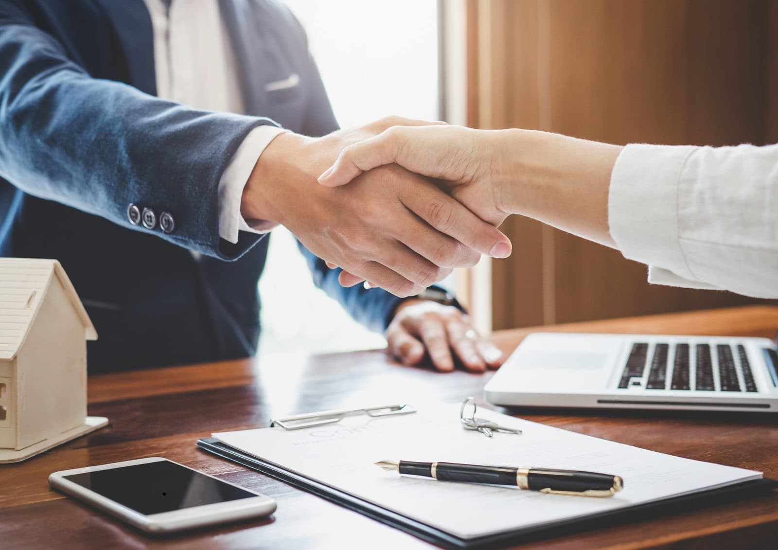 Professionals shaking hands over a desk with documents and a laptop
