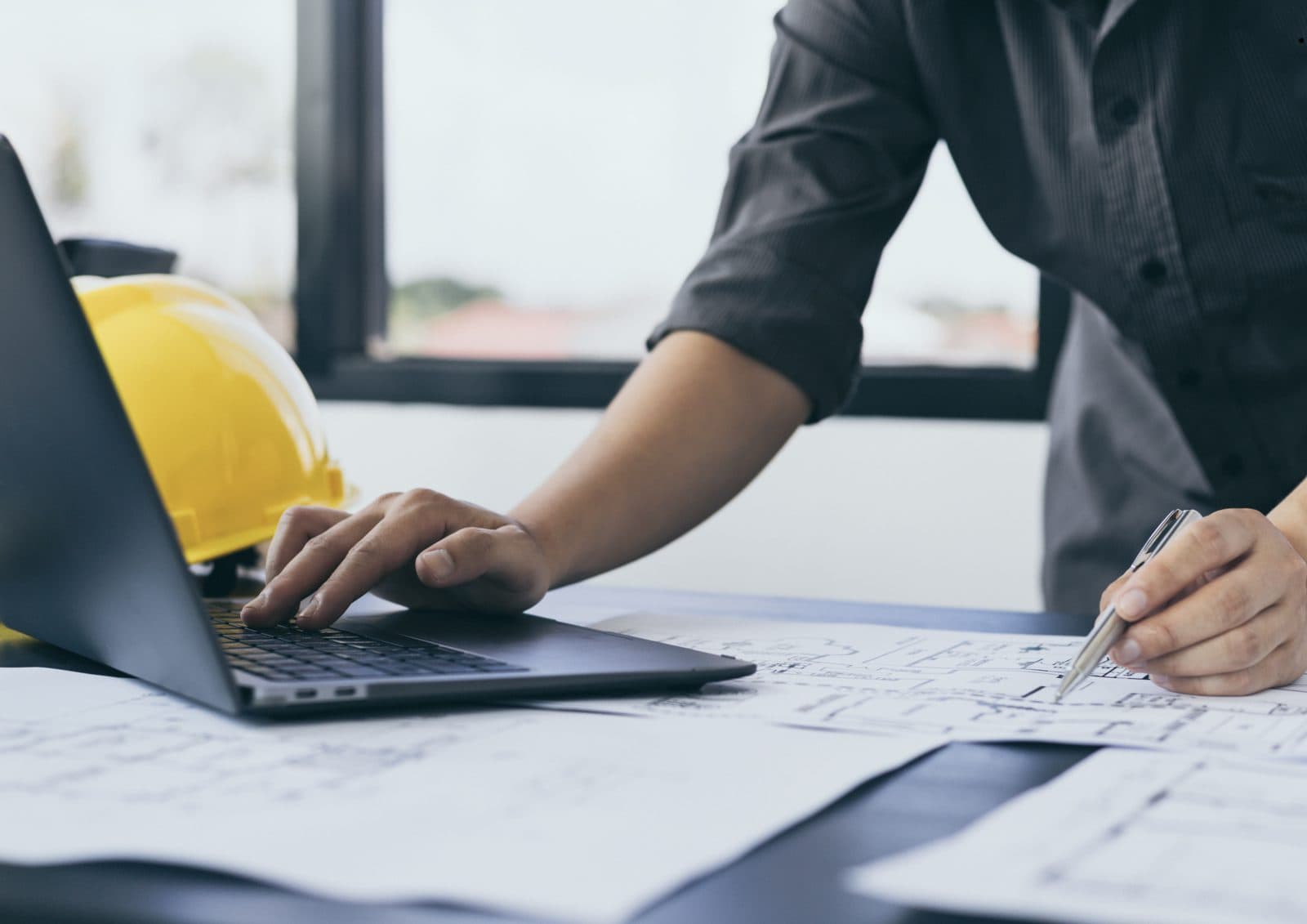Professional working on a laptop beside a hard hat and construction plans