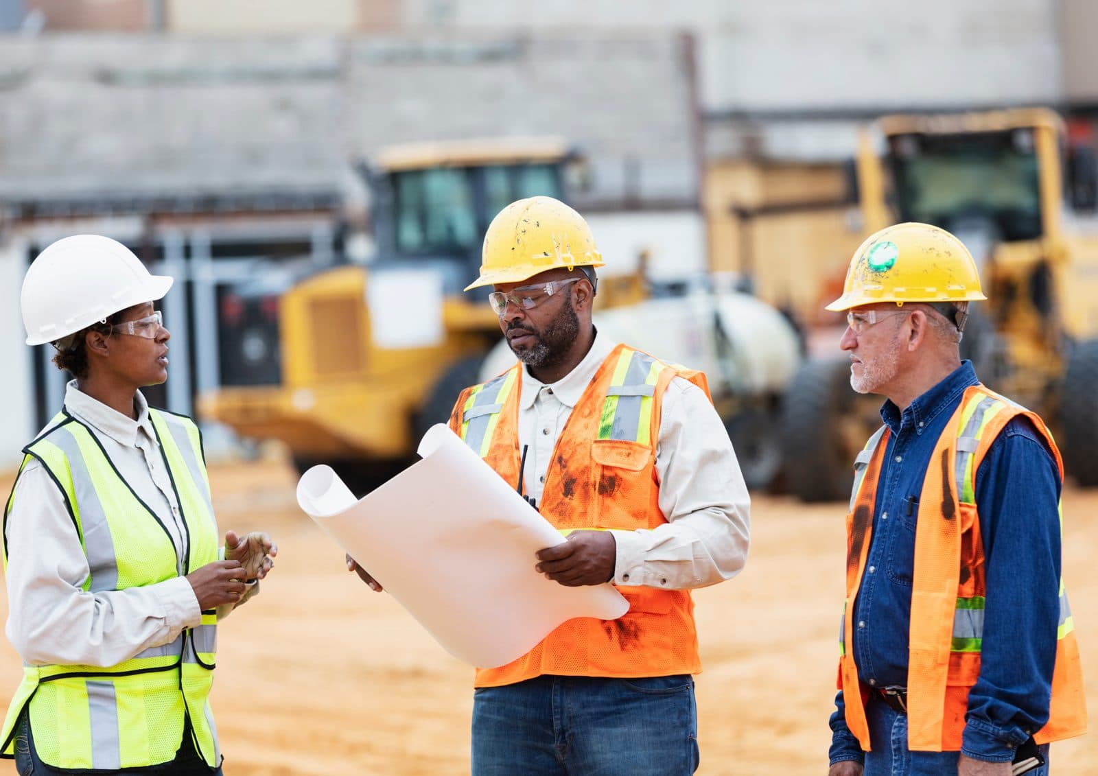 Three construction professionals in hard hats reviewing plans at a job site
